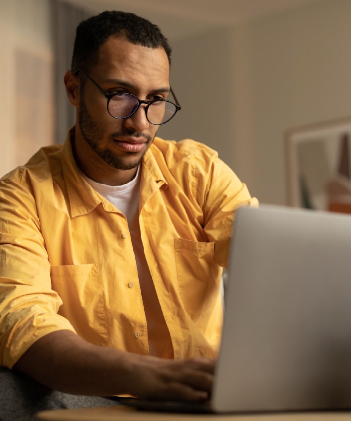 A man in a yellow shirt looking at his laptop which may be infected with spyware.